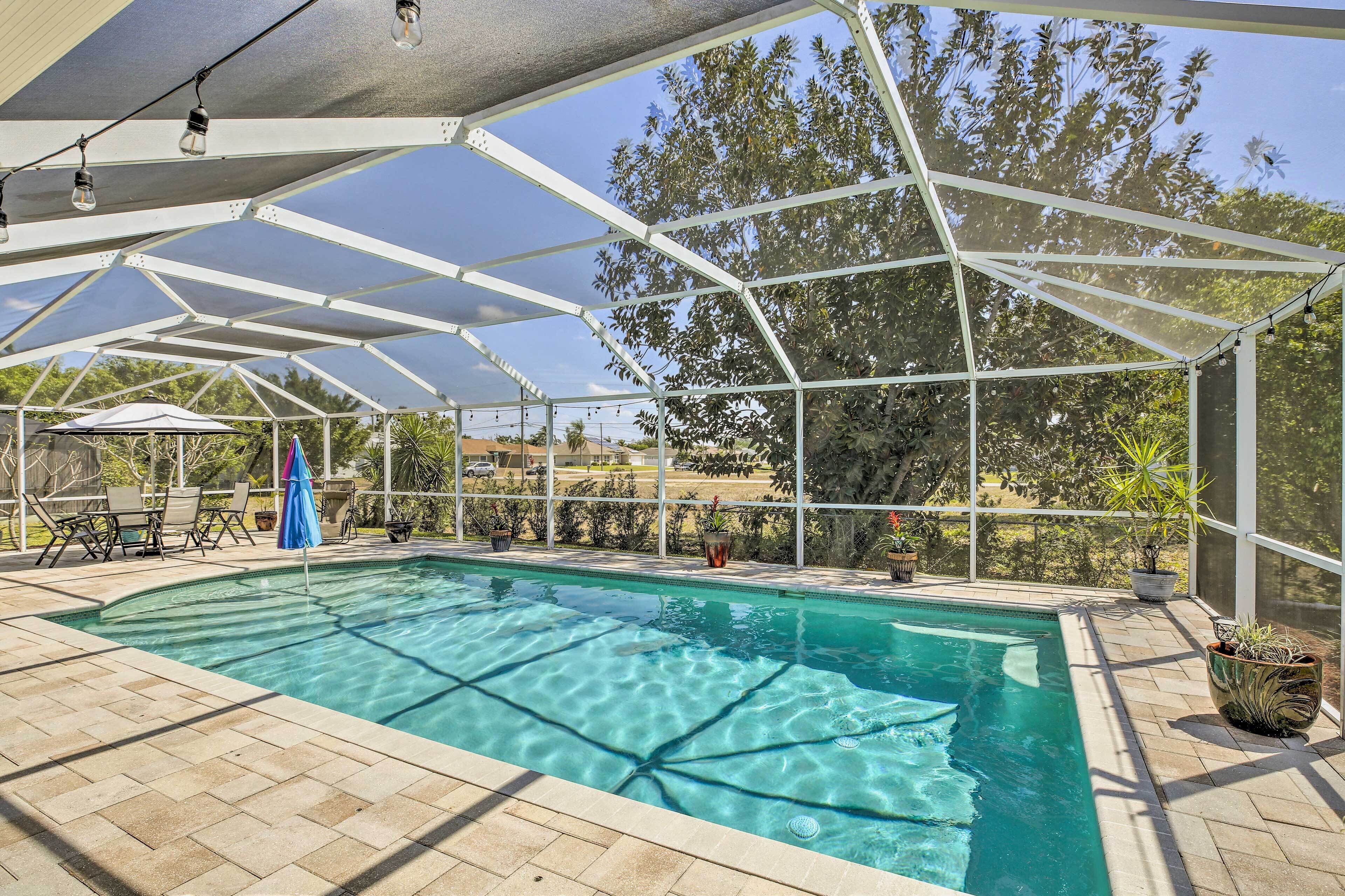 A covered swimming pool with a clear blue water surface, surrounded by lounge chairs and potted plants.