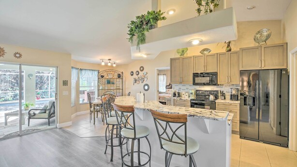 A modern kitchen with a central island, bar stools, stainless steel appliances, and decorative plants. - Lanai & Heated Pool: Stunning Cape Coral Getaway (Cape Coral)
