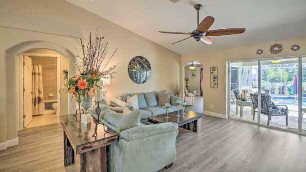 A spacious living room with a large ceiling fan, a sofa, a coffee table, and a view through glass doors to an outdoor patio area. - Lanai & Heated Pool: Stunning Cape Coral Getaway (Cape Coral)