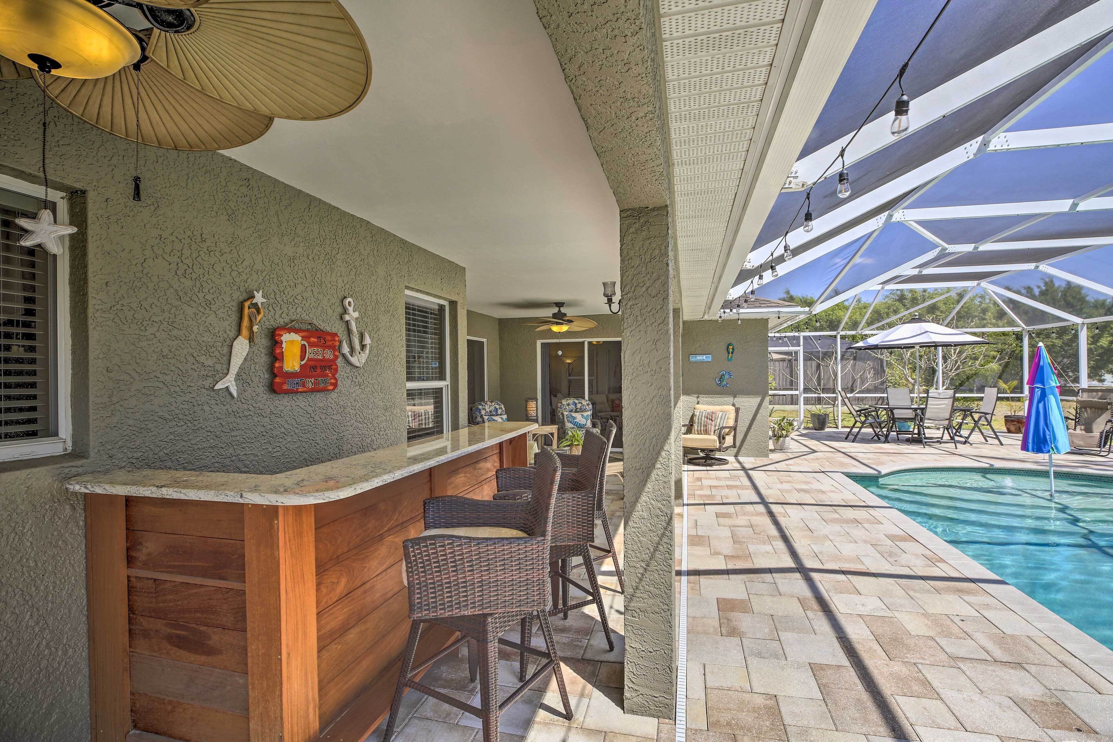 A poolside bar area with wicker chairs, a wooden counter, and a pool with a tiled deck.