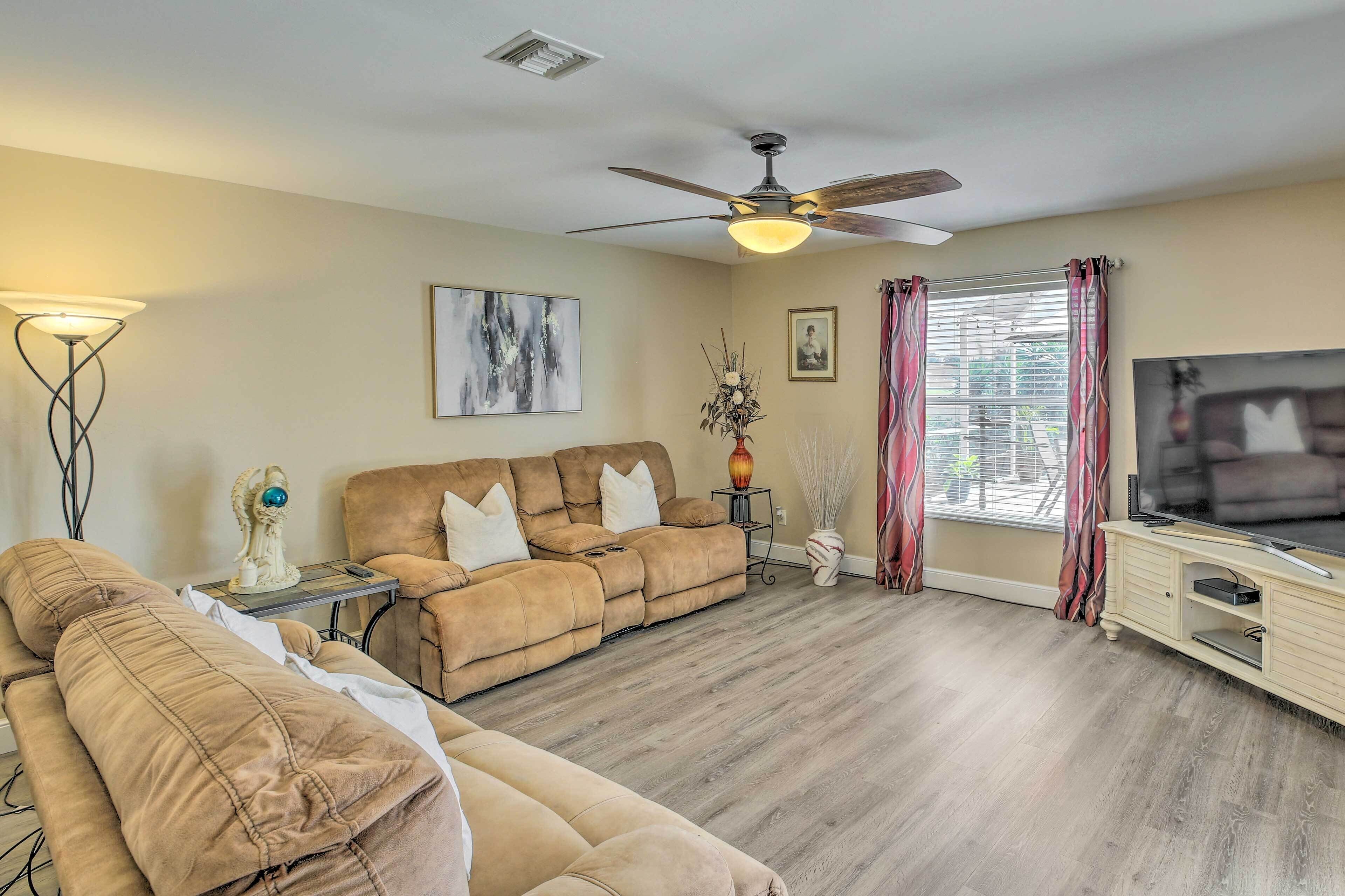 A living room with a sofa set, a television, a ceiling fan, and a window with curtains.