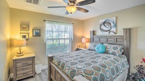 A bedroom with a bed, a nightstand, a ceiling fan, a window with blinds, and a wall with framed pictures. - Lanai & Heated Pool: Stunning Cape Coral Getaway (Cape Coral)