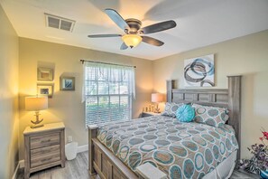 A bedroom with a bed, a nightstand, a ceiling fan, a window with blinds, and a wall with framed pictures. - Lanai & Heated Pool: Stunning Cape Coral Getaway (Cape Coral)