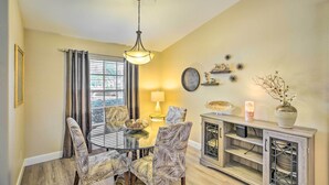 A dining area with a glass table, patterned chairs, a chandelier, a lamp, decorative items on a console, and a view through the window. - Lanai & Heated Pool: Stunning Cape Coral Getaway (Cape Coral)