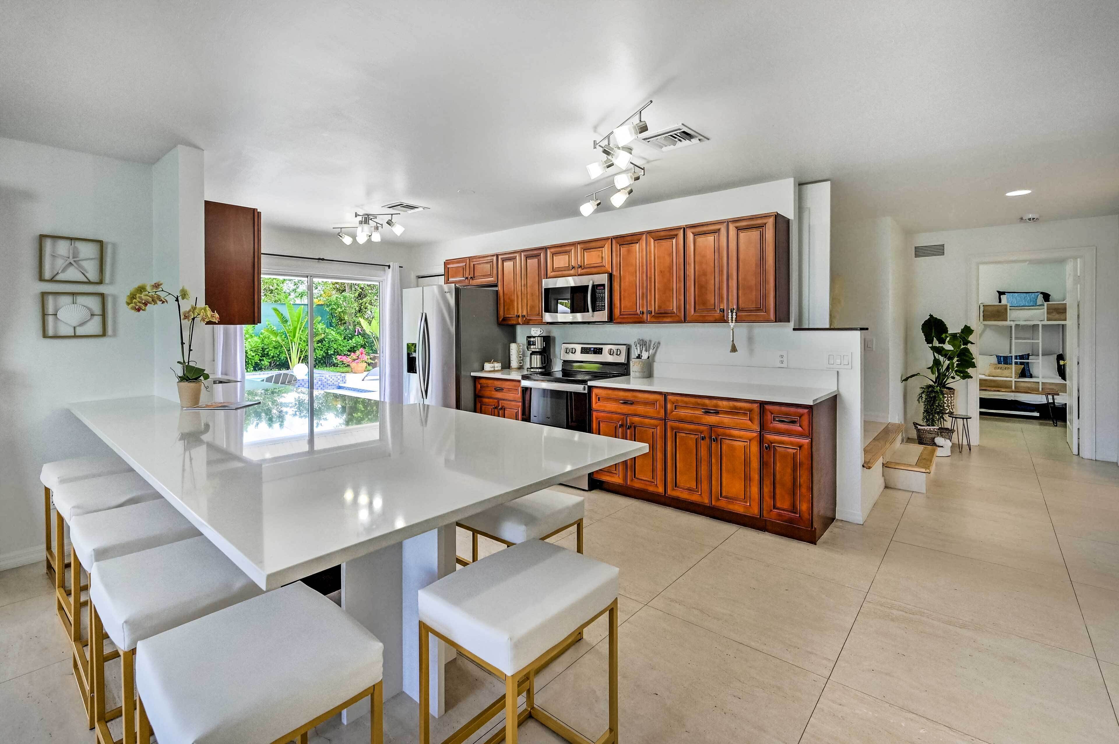 A modern kitchen with wooden cabinets, a large island with bar stools, and a view of greenery outside.