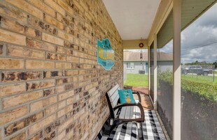 A covered porch with a brick wall, a bench, and a view of the street.
