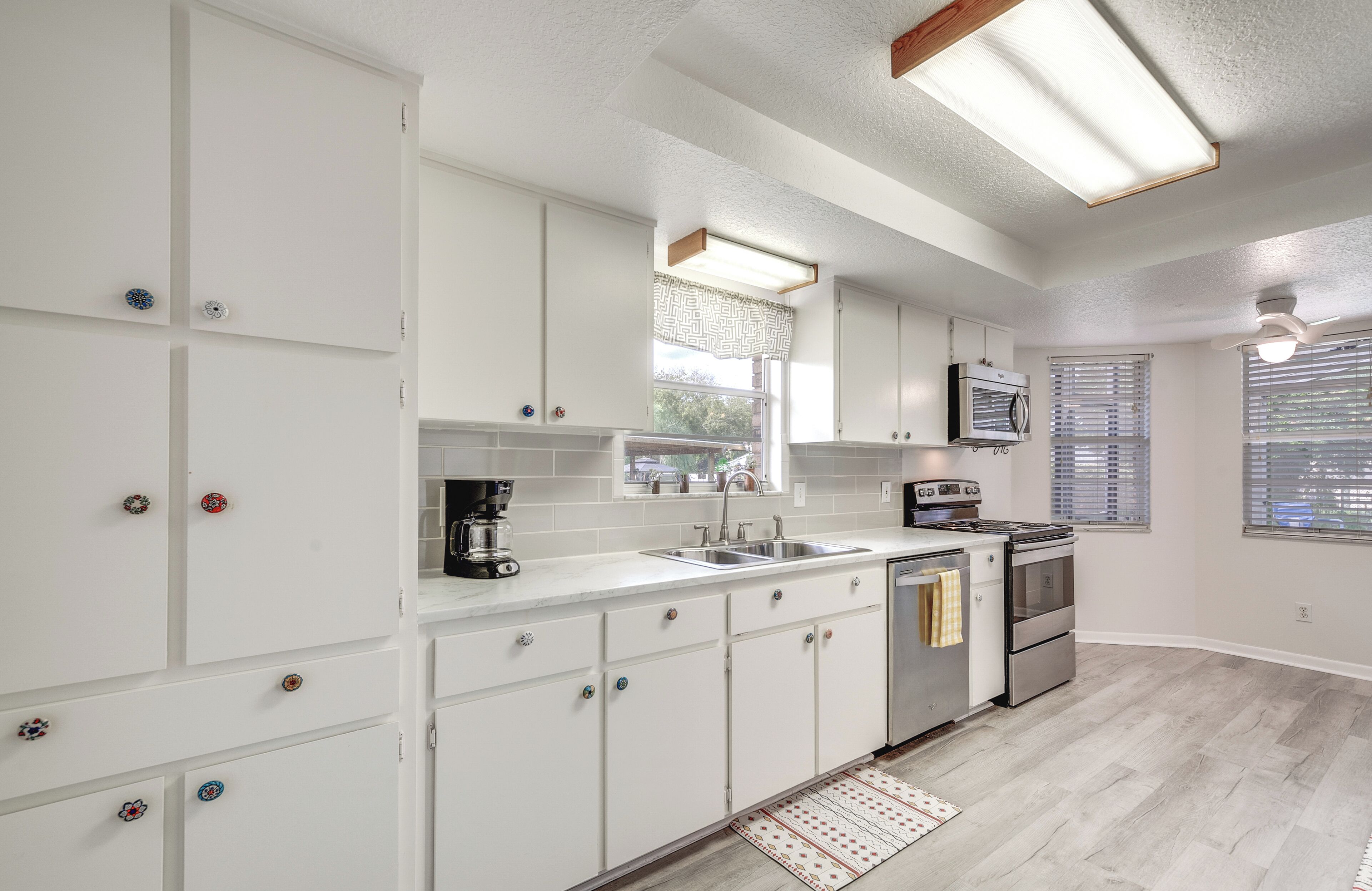 A modern kitchen with white cabinets, stainless steel appliances, and a window with blinds.