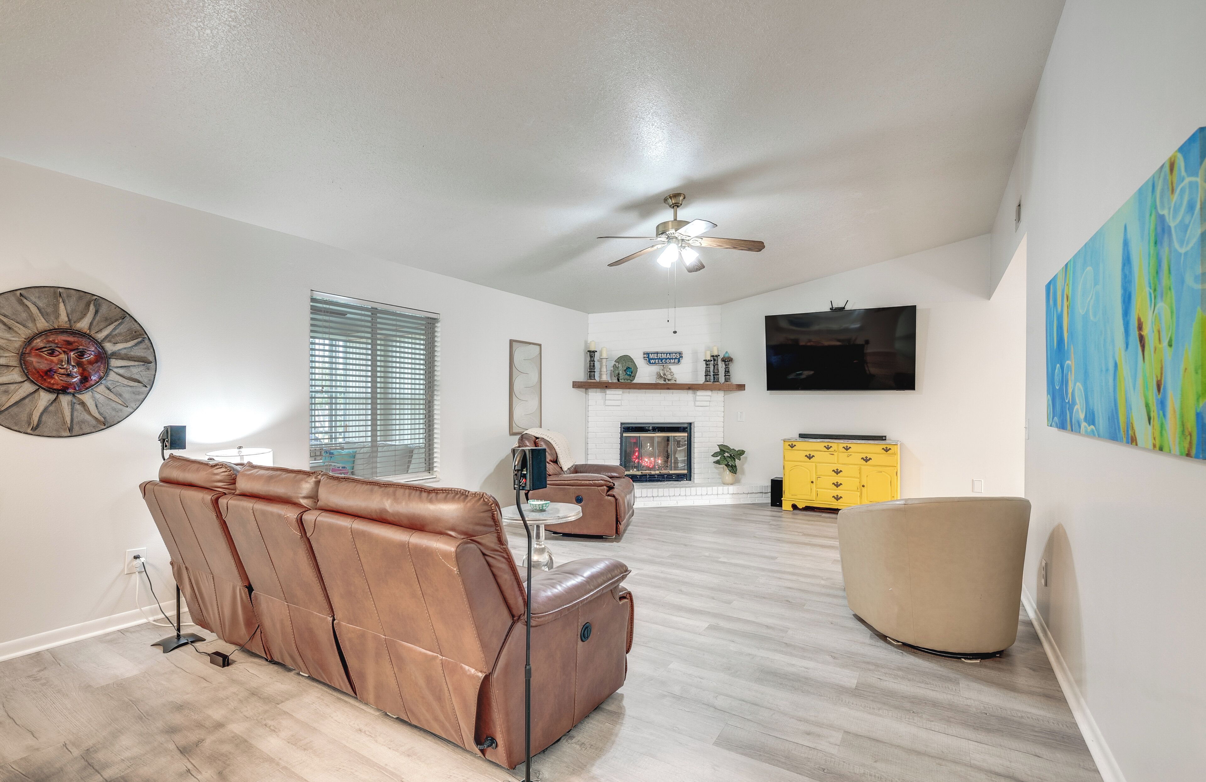 A spacious living room with a leather sofa, a round beige chair, and a flat-screen TV mounted on the wall.