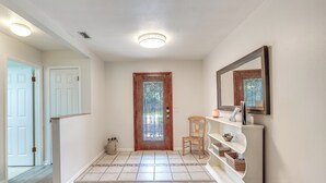 Um corredor com porta de madeira, parede branca, um espelho e uma prateleira com cestos.
