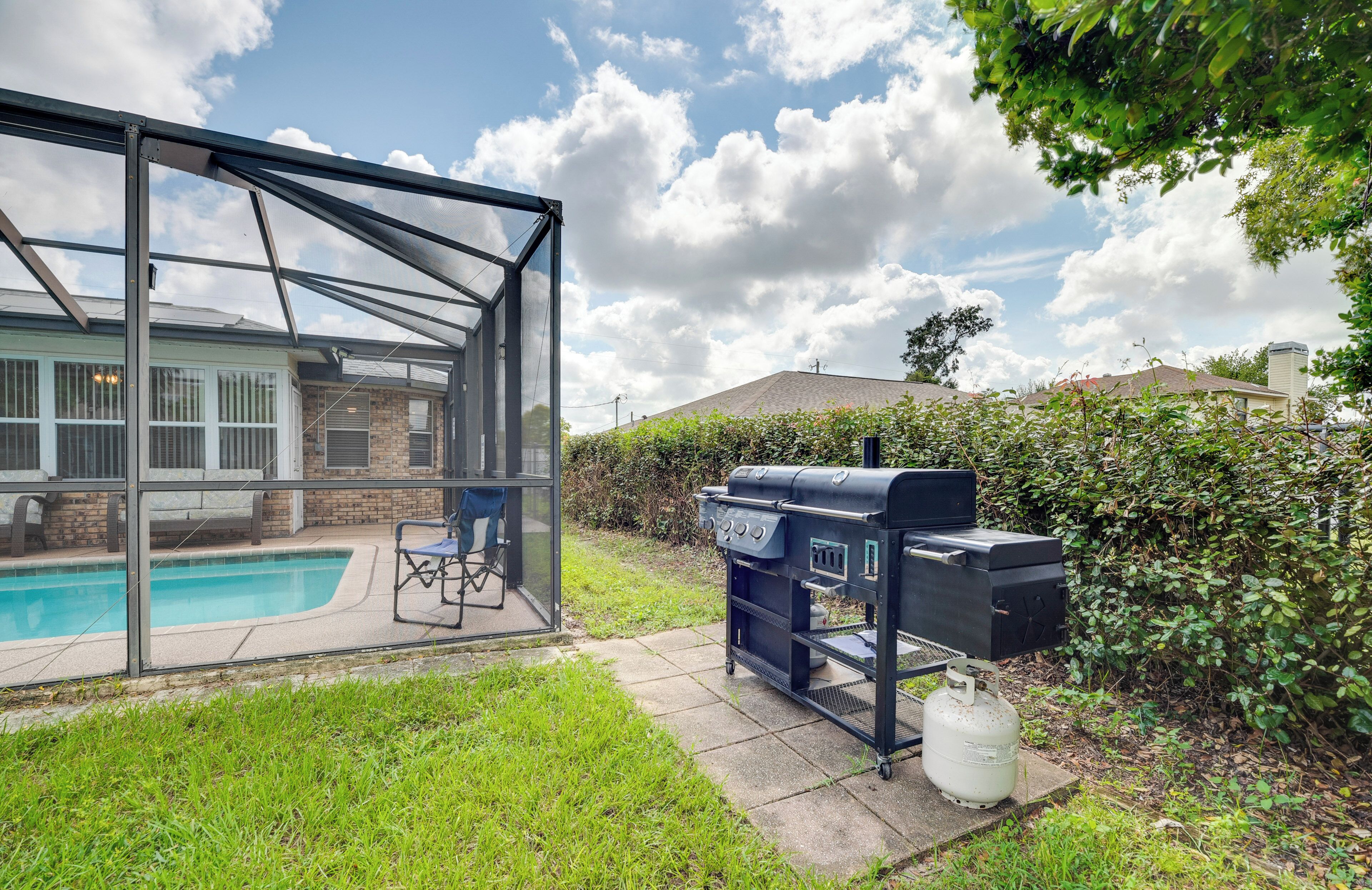 A backyard with a swimming pool, a covered patio, and a barbecue grill.