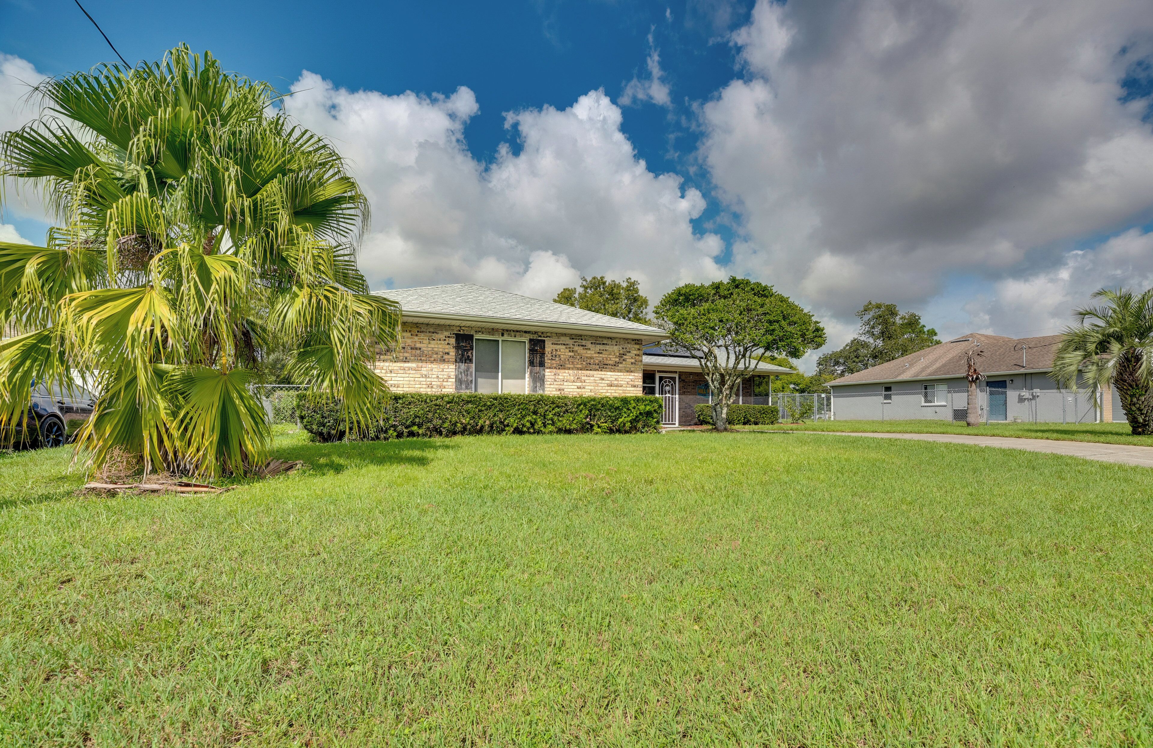 A residential house with a brick exterior, a well-maintained lawn, and a palm tree in the foreground.