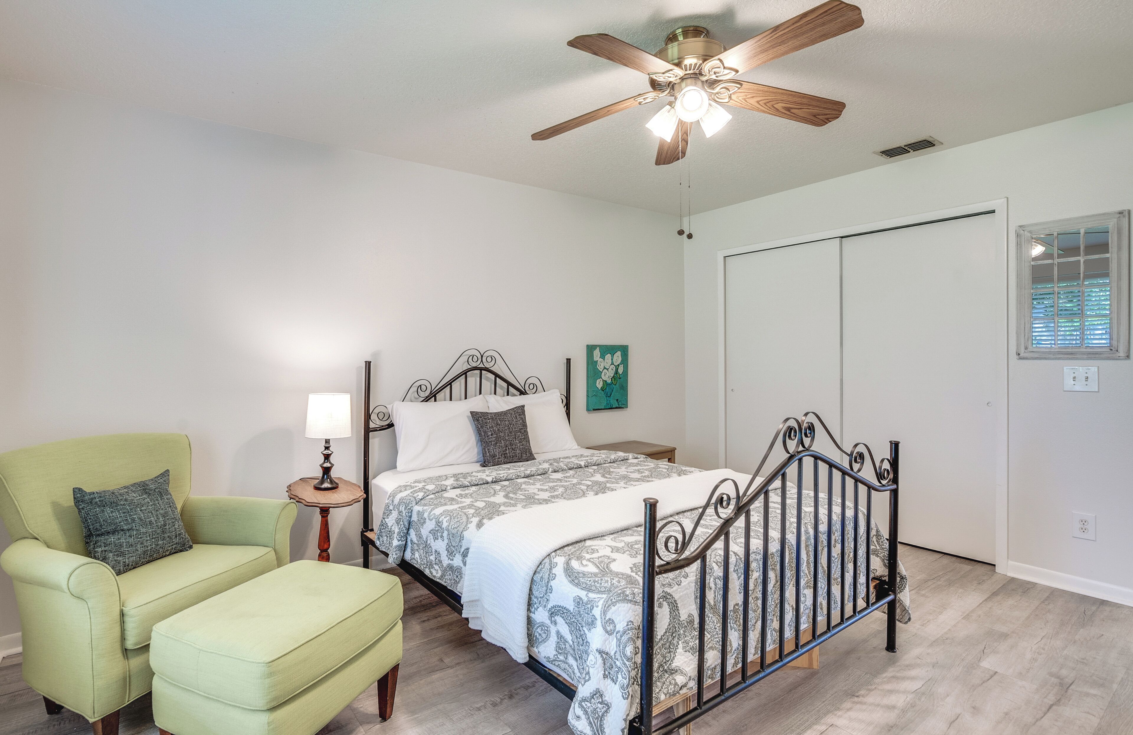 A bedroom with a bed, a chair, a nightstand, a ceiling fan, and a window.