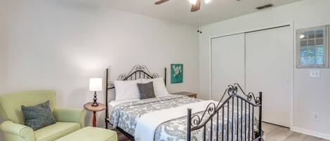 A bedroom with a bed, a chair, a nightstand, a ceiling fan, and a window.
