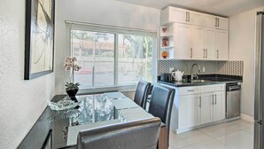 A modern kitchen with white cabinets, a black countertop, and a glass dining table with chairs. - Shady & Eclectic Fort Lauderdale Dwelling w/ Yard! (Fort Lauderdale)