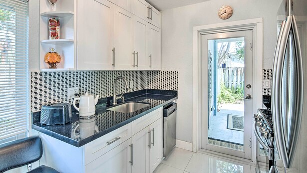 A modern kitchen with white cabinets, a black countertop, a stainless steel sink, a dishwasher, and a refrigerator. - Shady & Eclectic Fort Lauderdale Dwelling w/ Yard! (Fort Lauderdale)