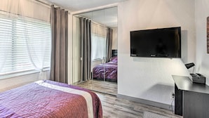 A bedroom with a bed, a TV mounted on the wall, a mirror, and a desk with a lamp. - Shady & Eclectic Fort Lauderdale Dwelling w/ Yard! (Fort Lauderdale)