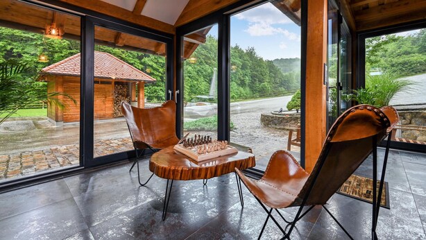 A spacious room with large windows offering a view of a wooden cabin and lush greenery. - Amazing home in Vitesinec with sauna (Vitesinec)