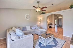 A living room with a sectional sofa, a coffee table, a ceiling fan, and a clock on the wall. - Family-friendly Home ~ 6 Mi to Beach or Golf (Edgewater)