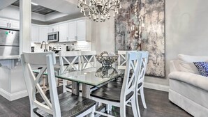 Une cuisine moderne avec des meubles blancs, un réfrigérateur en acier inoxydable et un coin repas comprenant une table en verre et des chaises blanches.