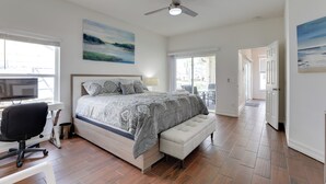 Een slaapkamer met een bed, een bureau, een stoel, een plafondventilator en kunstwerken aan de muren.