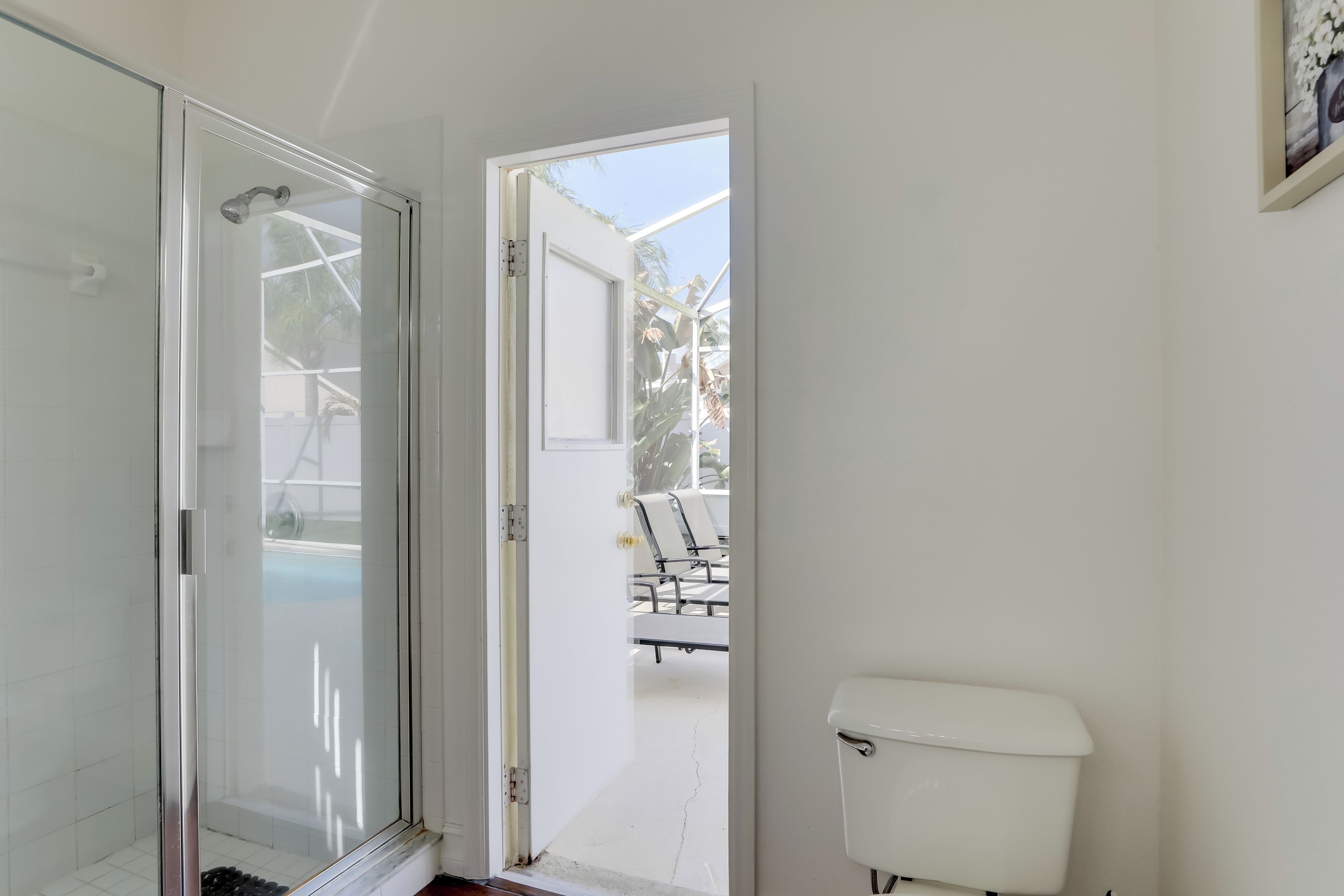 Une salle de bain dotée d’une porte de douche en verre, de toilettes et offrant une vue sur un espace extérieur aménagé avec des chaises et une table.