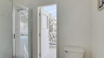 Une salle de bain dotée d’une porte de douche en verre, de toilettes et offrant une vue sur un espace extérieur aménagé avec des chaises et une table.