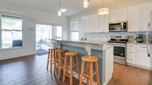 Een moderne keuken met witte kasten, een centraal eiland met krukken, roestvrijstalen apparatuur en grote ramen.