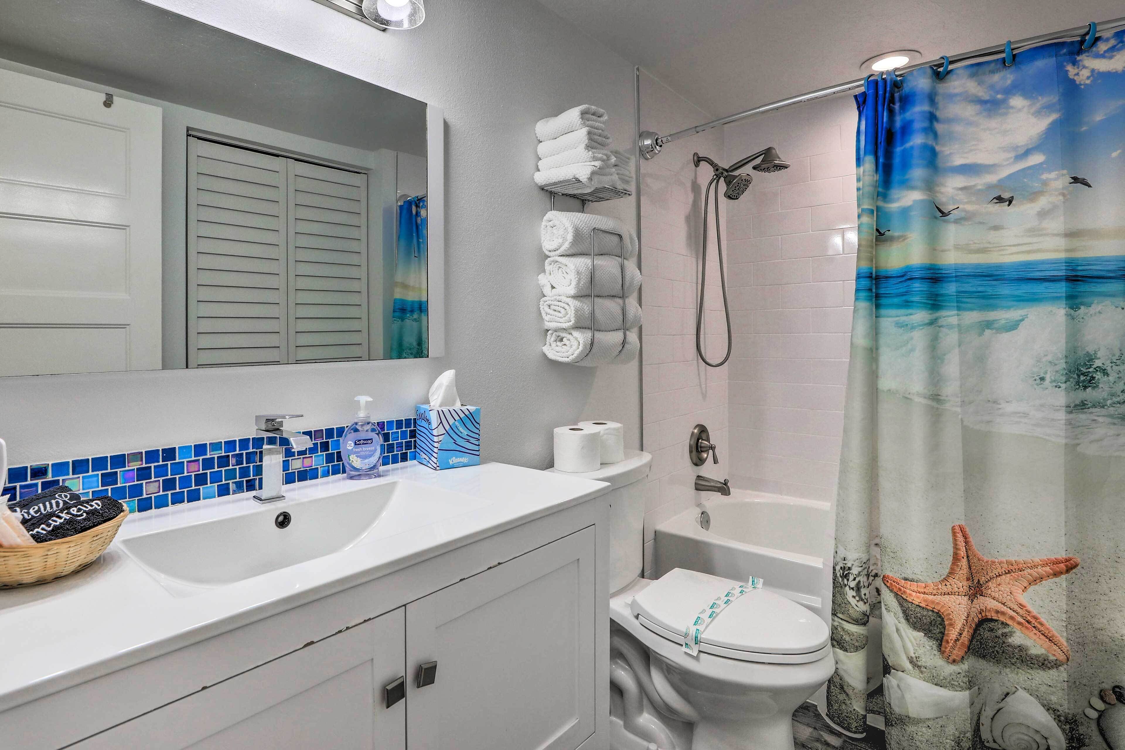 A bathroom with a white sink, mirror, and toilet. There are towels stacked on the wall and a shower curtain with a sea theme.