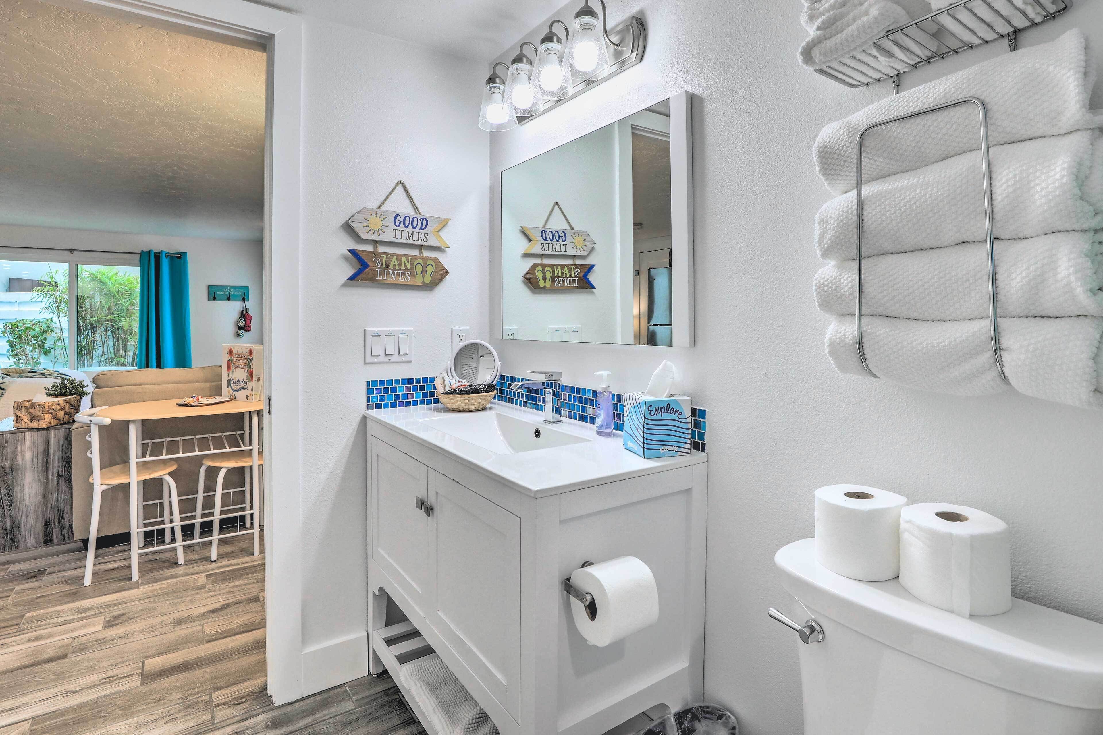 Een badkamer met een witte wastafel, spiegel en toilet. Handdoeken hangen aan de muur, er staat een klein tafeltje met stoelen en er is uitzicht naar buiten.