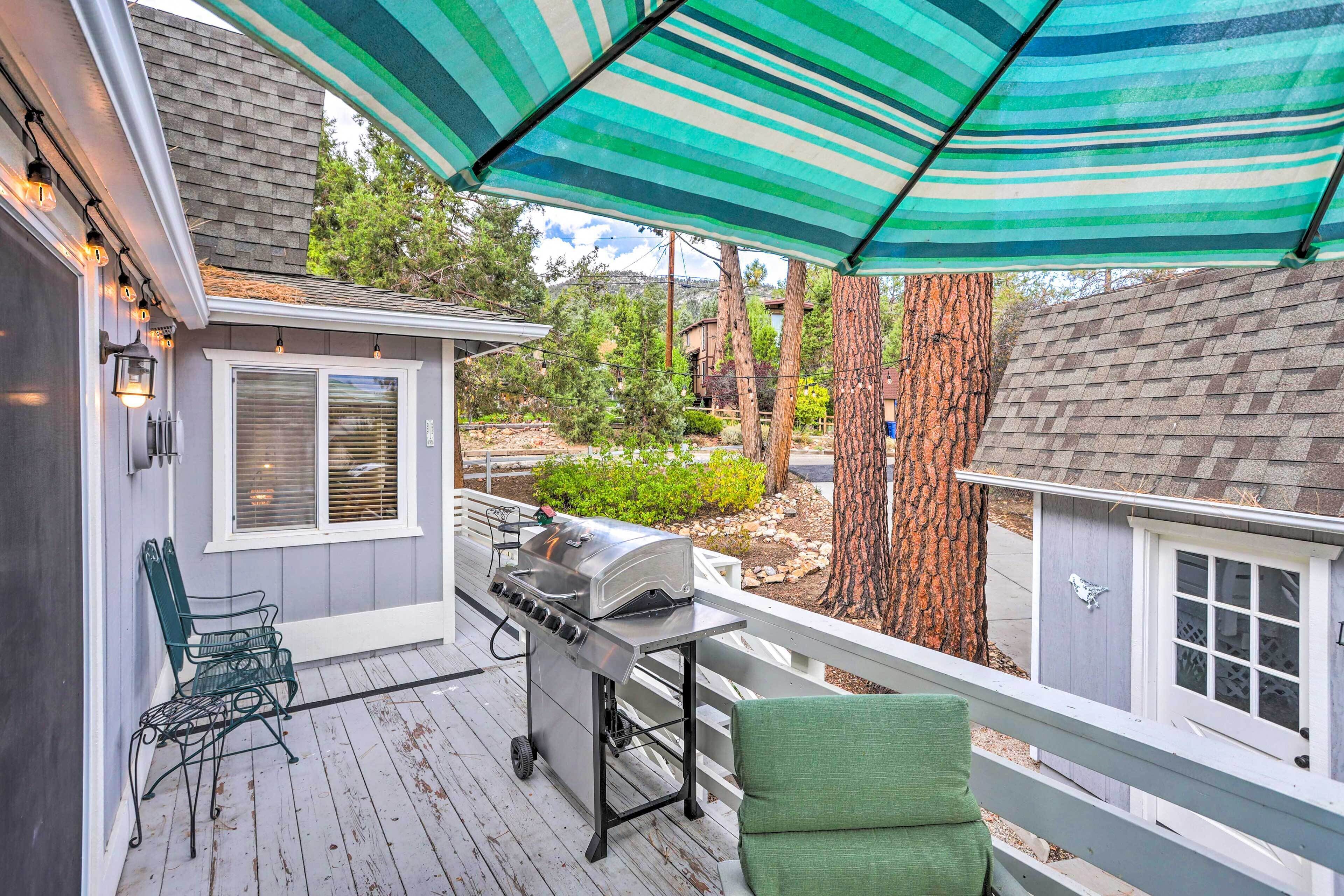 A covered outdoor patio with a grill, chairs, and a view of the surrounding landscape.