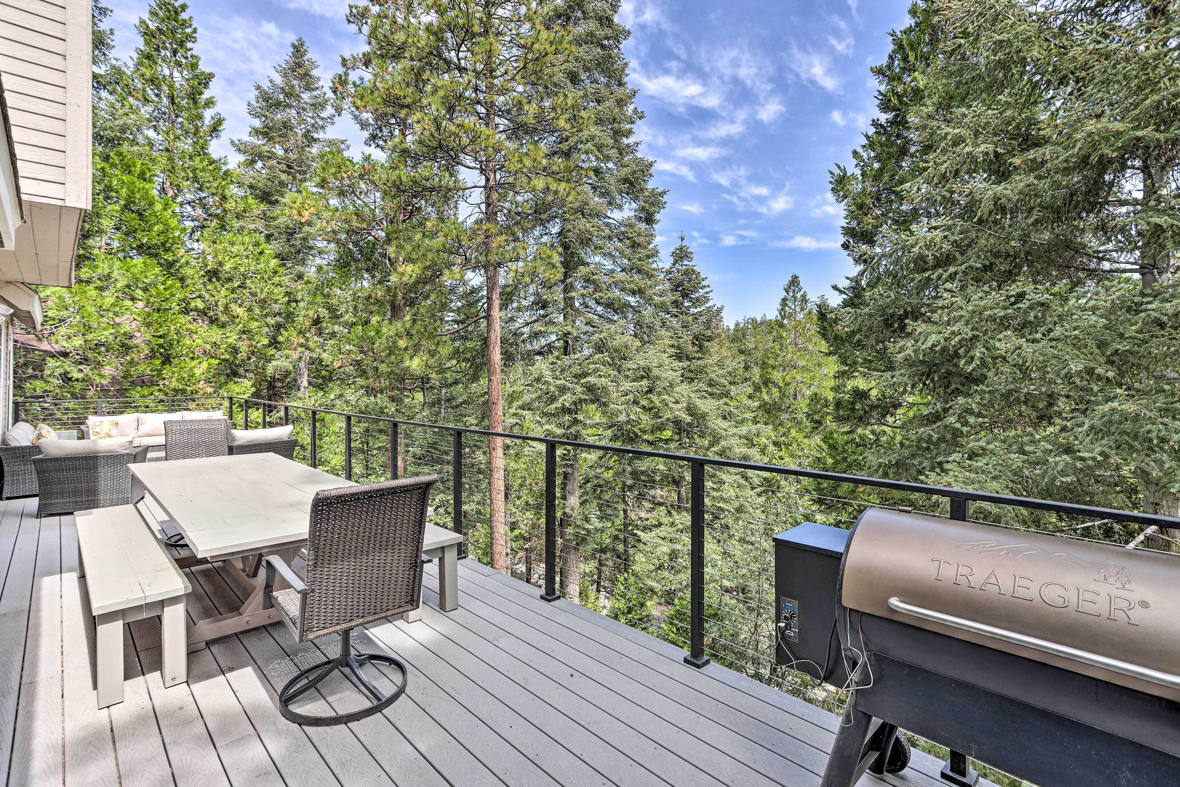A deck with a table and chairs, a grill, and a view of tall trees.
