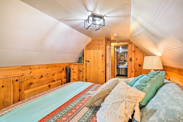 Un dormitorio acogedor en el ático con paredes de madera, techo inclinado y cama con ropa de cama estampada.