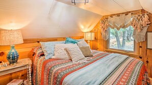 Ein gemütliches Schlafzimmer mit einem Holzkopfteil, einer gemusterten Tagesdecke und einem Fenster mit Makramee-Vorhängen.