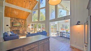 A spacious kitchen with a large island, stone fireplace, and high ceilings with wooden beams.