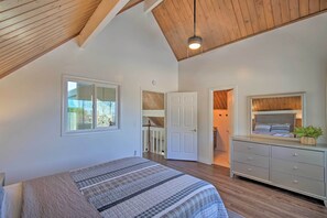 Un dormitorio con techo inclinado, una cama con colcha a rayas, un aparador y un espejo que refleja una cama.