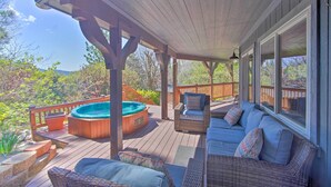 A covered deck with a hot tub, wicker furniture, and a view of the surrounding trees.