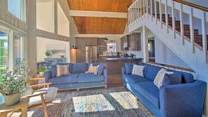A spacious living area with a high ceiling, a staircase, and a kitchen in the background.