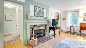 A room with a brick fireplace, a television, a wooden table, and a window with curtains. - Game Room + Patio: Quiet Centerville Beach Base (Centerville)