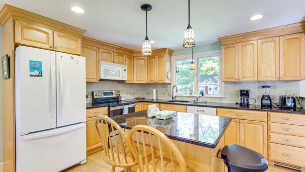 A kitchen with wooden cabinets, a white refrigerator, a microwave, a sink, and two bar stools. - Game Room + Patio: Quiet Centerville Beach Base (Centerville)
