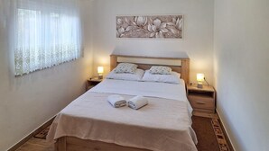 A neatly made bed with a white bedspread and two pillows, two bedside lamps, a decorative wall piece above the bed, and a patterned rug on the floor. - Gorgeous apartment in Starigrad with WiFi (Starigrad)