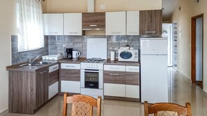 A compact kitchen with a gas stove, a built-in oven, a microwave, and a refrigerator. There are wooden cabinets and a window with curtains. - Gorgeous apartment in Starigrad with WiFi (Starigrad)