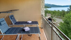 A balcony with two reclining chairs and a stone chimney, overlooking a lake and mountains. - Gorgeous apartment in Starigrad with WiFi (Starigrad)