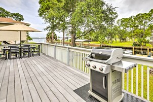 Una terraza de madera con una parrilla, asientos al aire libre y vistas a un lago.