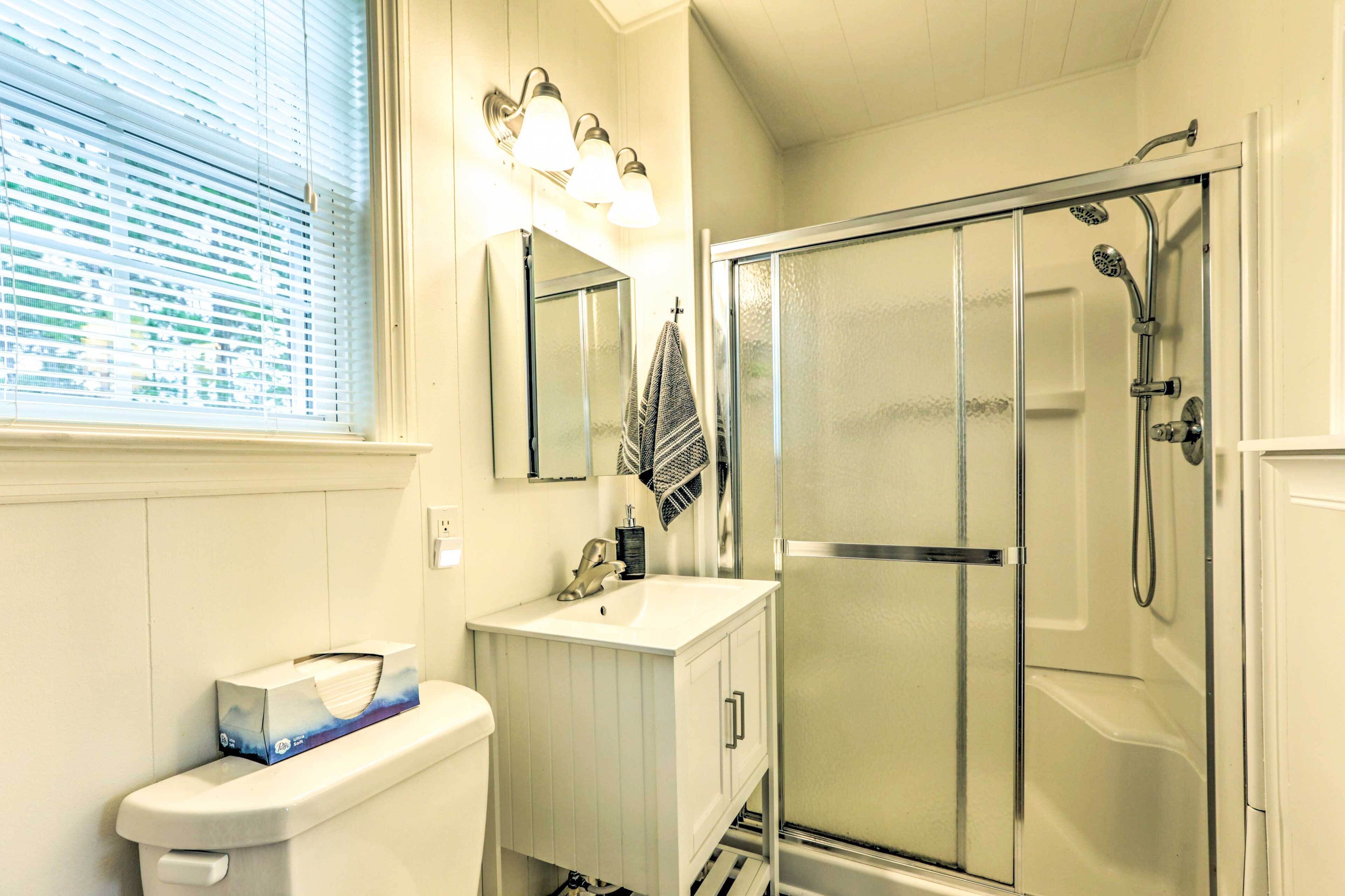 A bathroom with a toilet, sink, mirror, towel rack, and a glass-enclosed shower stall.