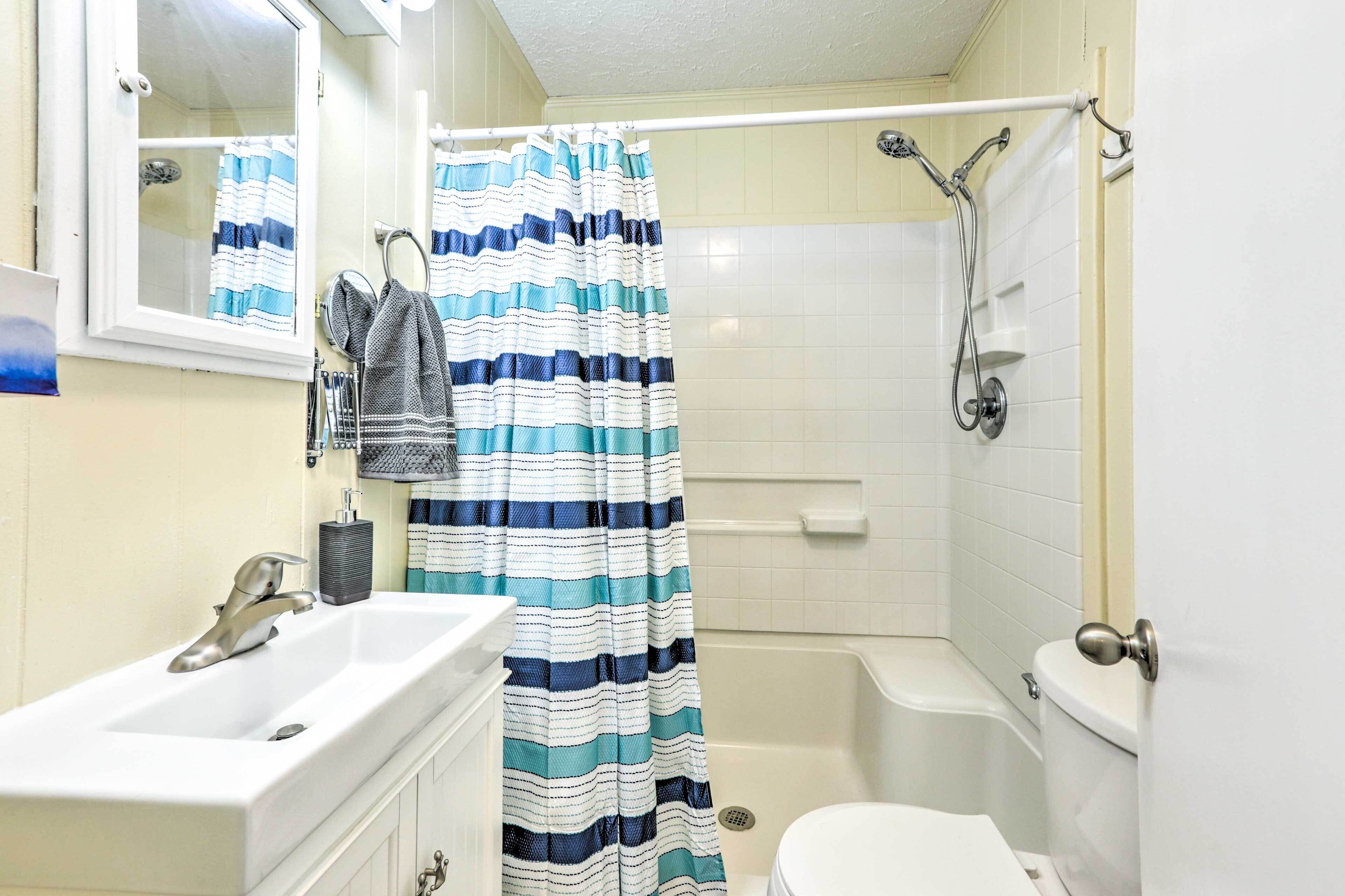 A bathroom with a white sink, a mirror, a striped shower curtain, a bathtub, and a toilet.