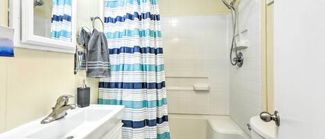 A bathroom with a white sink, a mirror, a striped shower curtain, a bathtub, and a toilet.