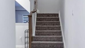 Un escalier avec des rampes en bois et des marches recouvertes de moquette, menant à un palier.
