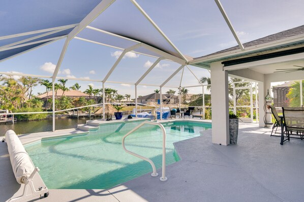 A covered outdoor swimming pool with a clear view of the surrounding landscape, including palm trees and a distant building.