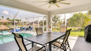 A covered patio with a pool, outdoor seating, and a ceiling fan. - Canal-front Cape Coral Home Rental: Pool, Lanai! (Cape Coral)