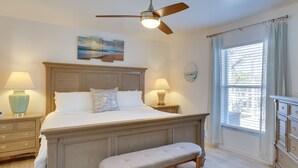 A bedroom with a large bed, two bedside tables, a bench, a ceiling fan, and a window with curtains. - Canal-front Cape Coral Home Rental: Pool, Lanai! (Cape Coral)